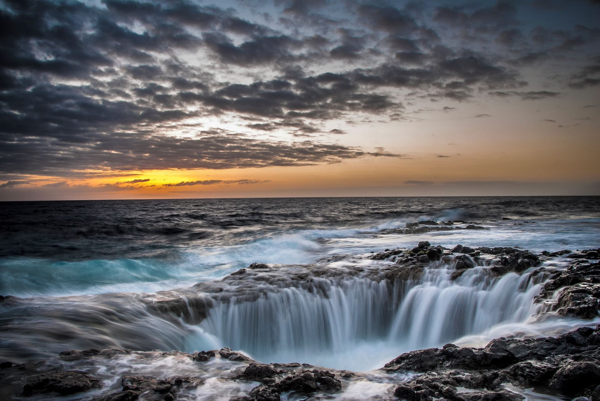 Olas del mar rompiendo sobre roca volcánica al atardecer